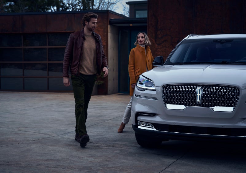A man and a woman approaching a 2024 Lincoln Aviator® SUV, which illuminates certain lights when they are close | Gates Ford Lincoln in Richmond KY