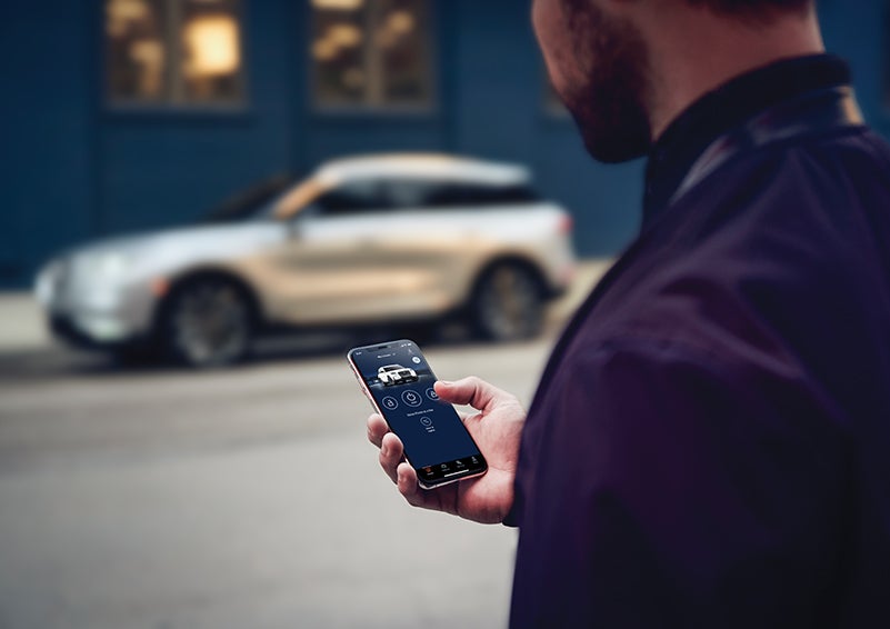 A person is shown interacting with a smartphone to connect to a Lincoln vehicle across the street. | Gates Ford Lincoln in Richmond KY
